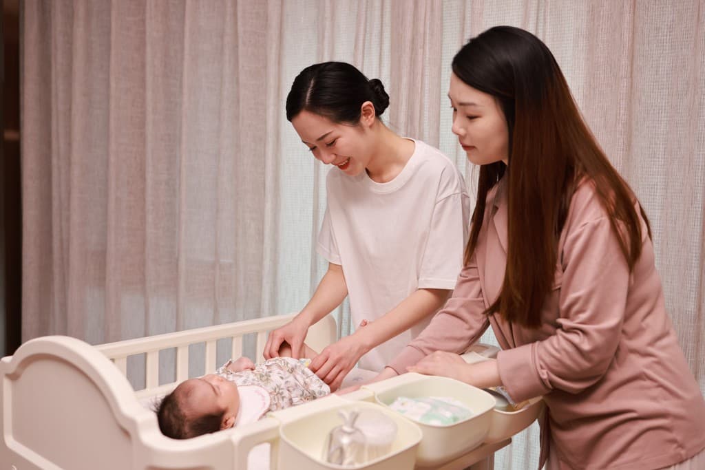 Two postpartum doulas settling a newborn into a crib