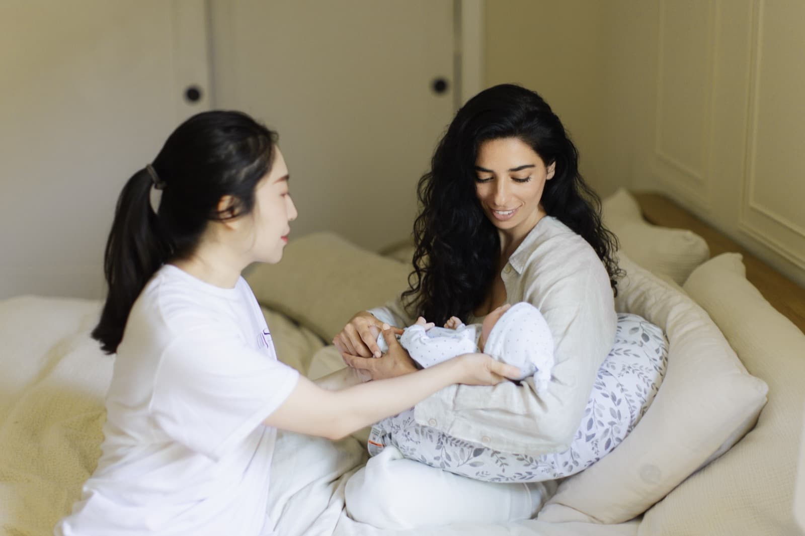A doula handing a swaddled newborn to the mother in bed